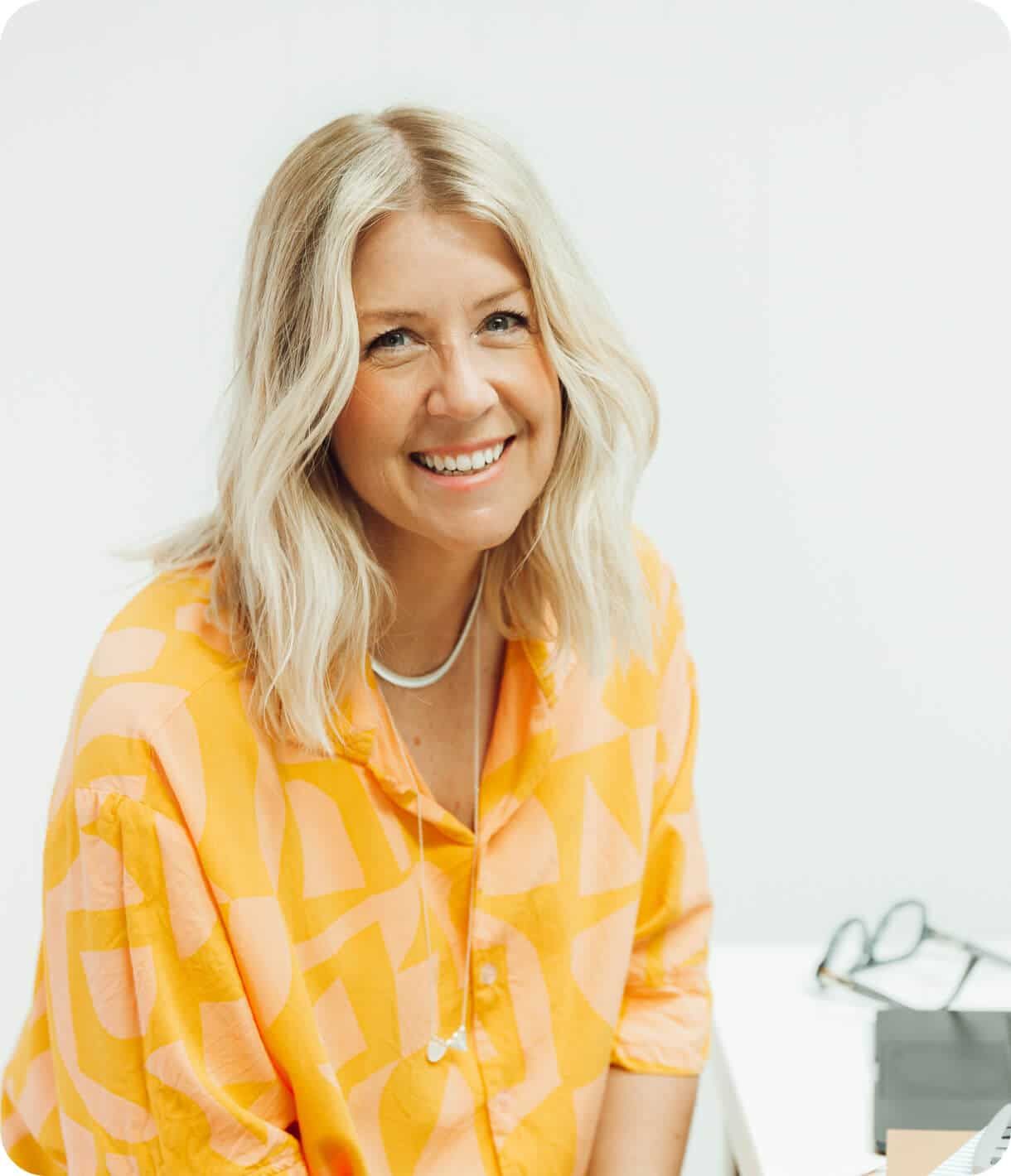 A picture of the company founder, wearing an orange shirt, smiling at the camera. She is showing her enthusiasm for her work.